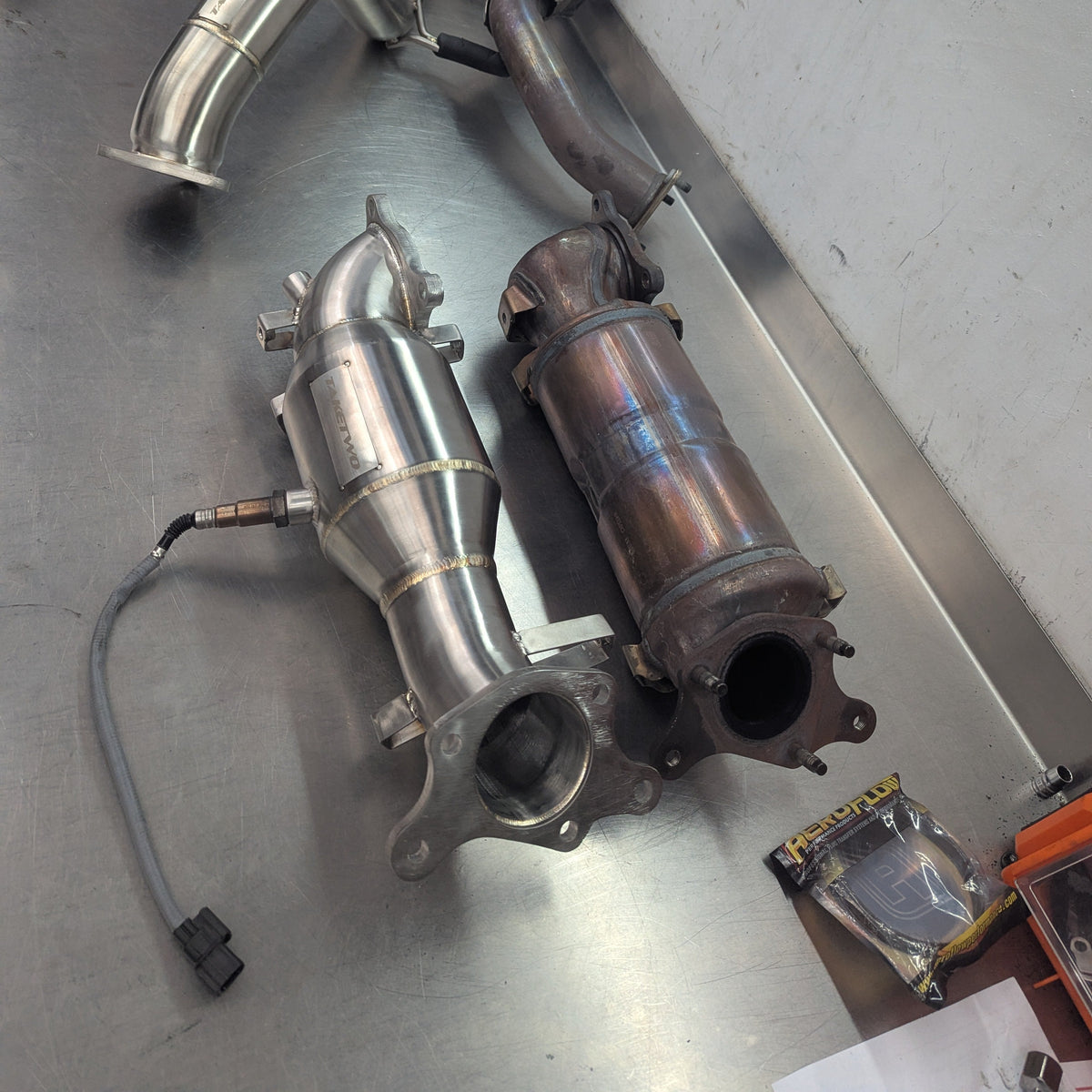 Metallic exhaust pipes on a workshop bench with tools in the background